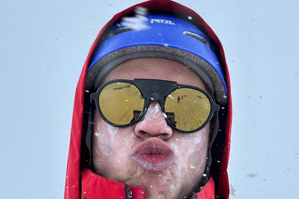 Egor on Mount Elbrus in a red jacket and blue helmet, face frosted, pulling a face at the camera.